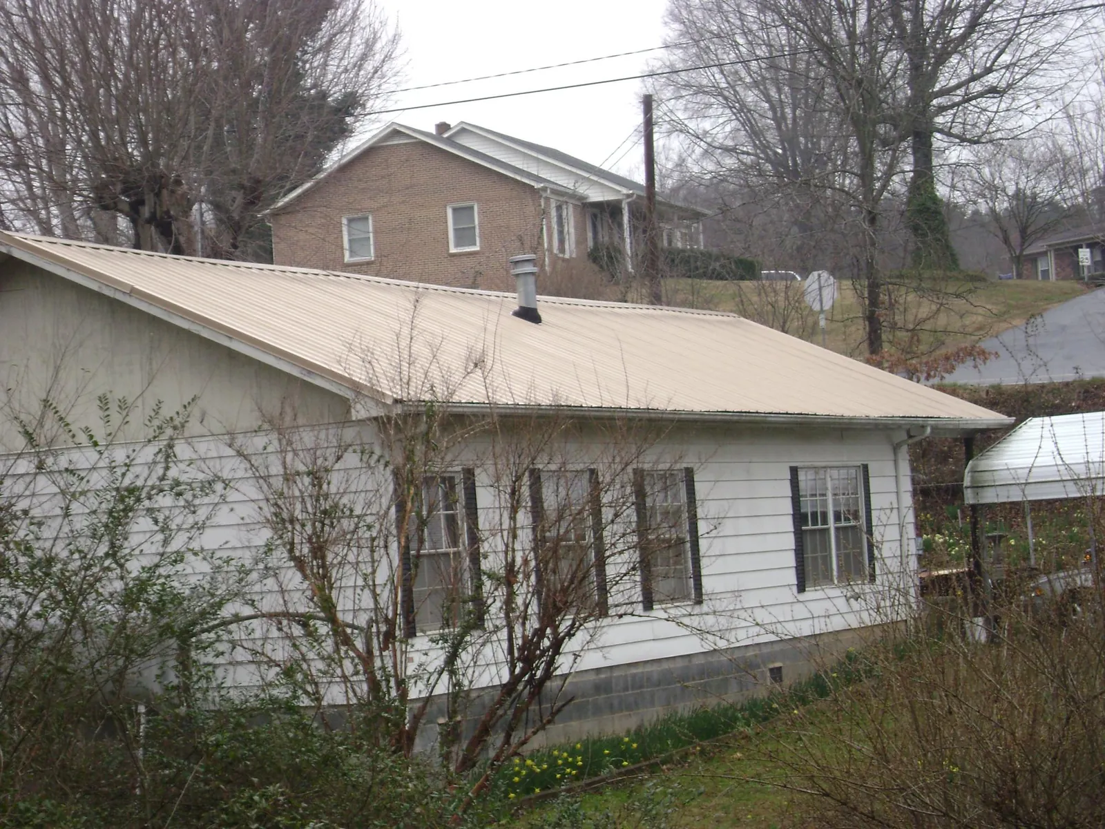 Tan metal roof on a white sided house set into a hillside — Commercial Roofing by Roofing Brothers in Sullivan